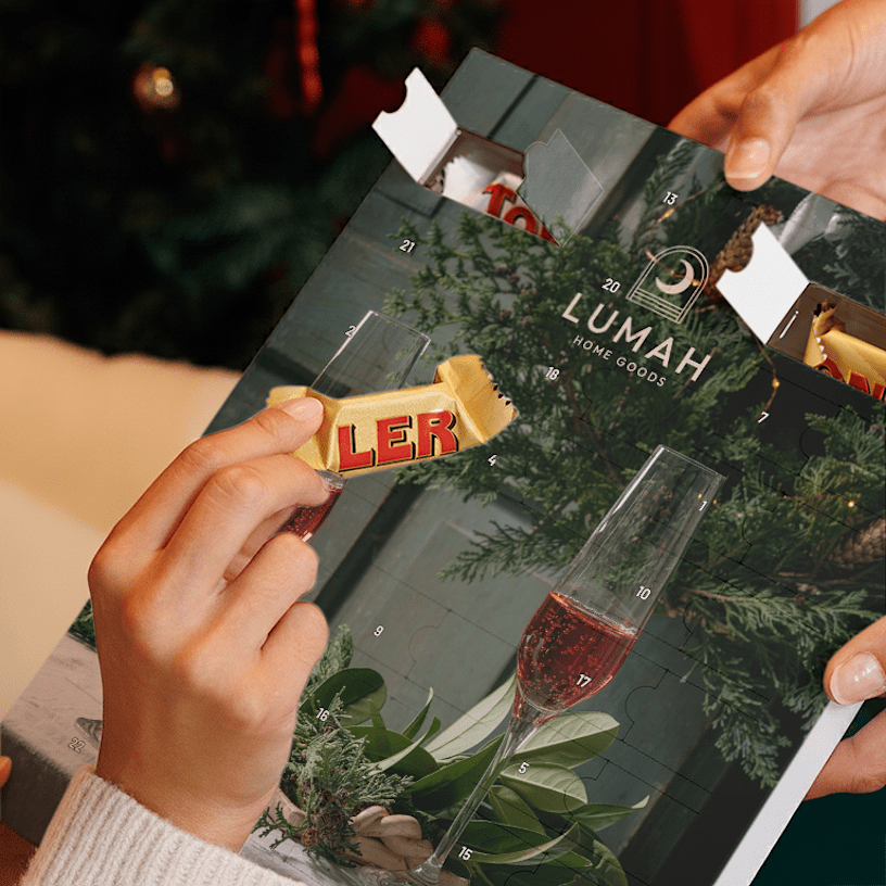 "Person taking out a small Toblerone chocolate from a custom advent calendar featuring the logo of a home decor business Lumah.  "