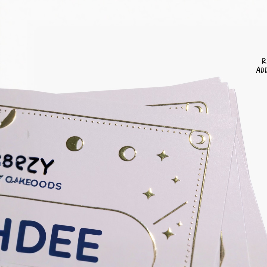 A close-up image of a business card featuring a gold raised foil logo and text.