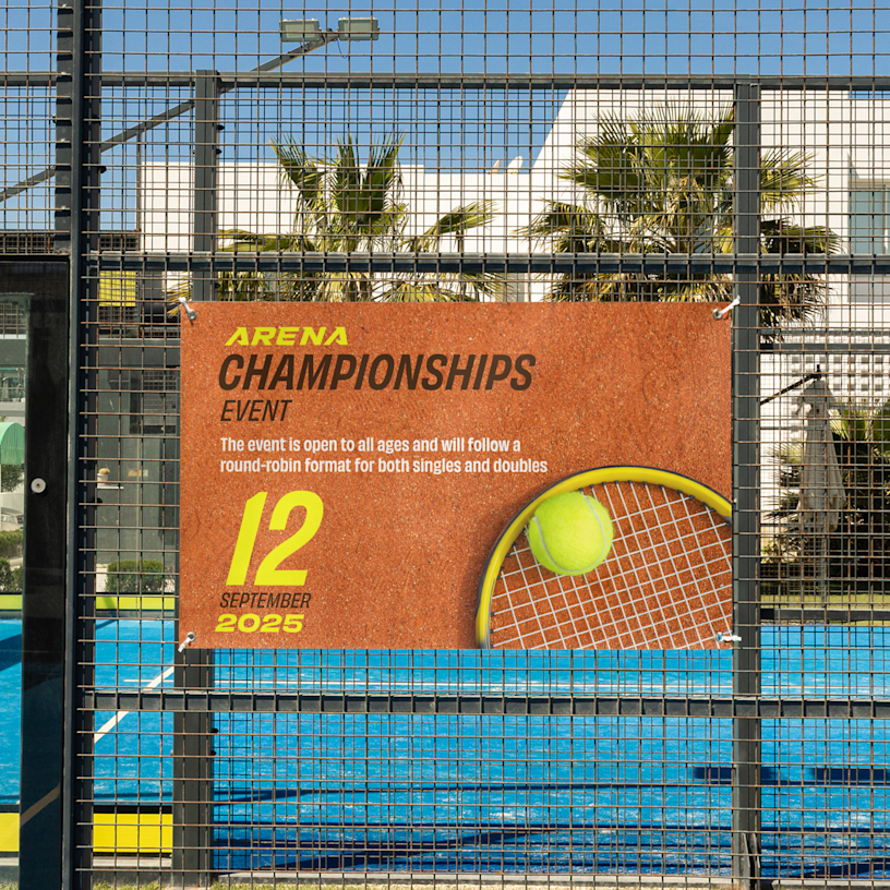 A standard banner for a tennis tournament hangs from its grommets on the fence of the court.