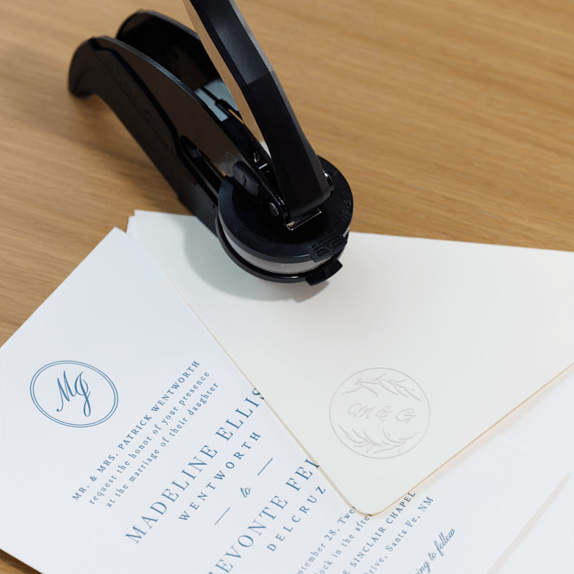 An embossing stamp and wedding stationery are placed together, with the stamp creating a matching, raised impression on the personalised envelope.
