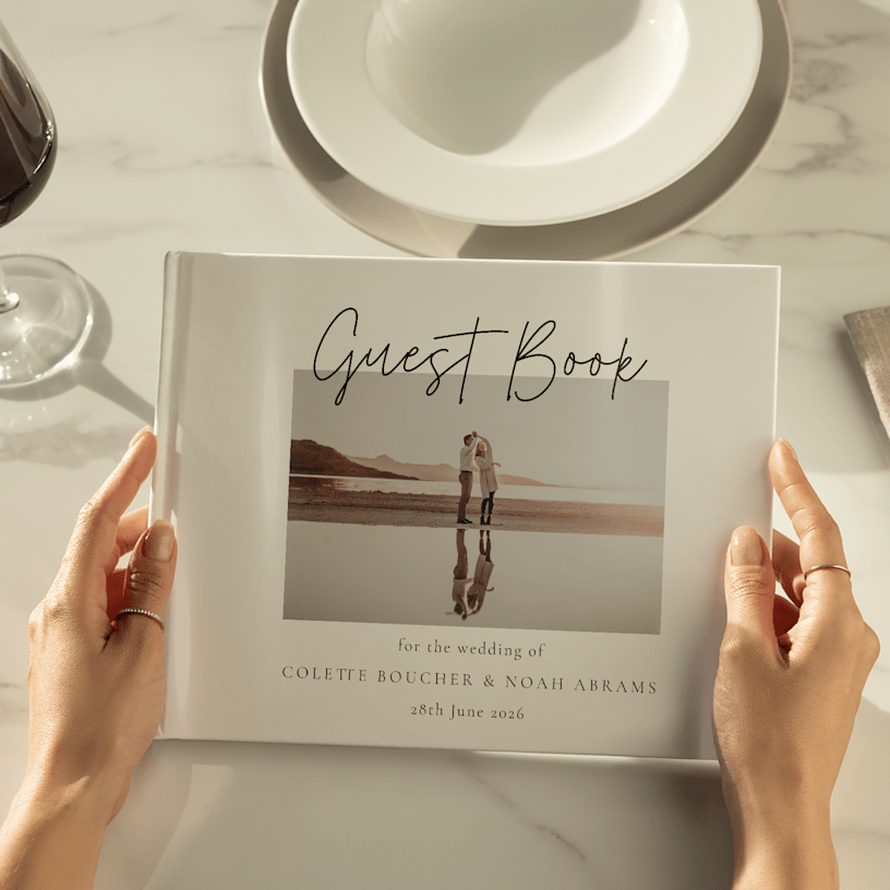 Hands holding a wedding guest book personalised with a photo of the couple on the cover. 