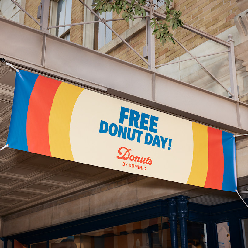 A banner with the message ‘FREE DONUT DAY!’ written big and bold, hung outside a doughnut shop.