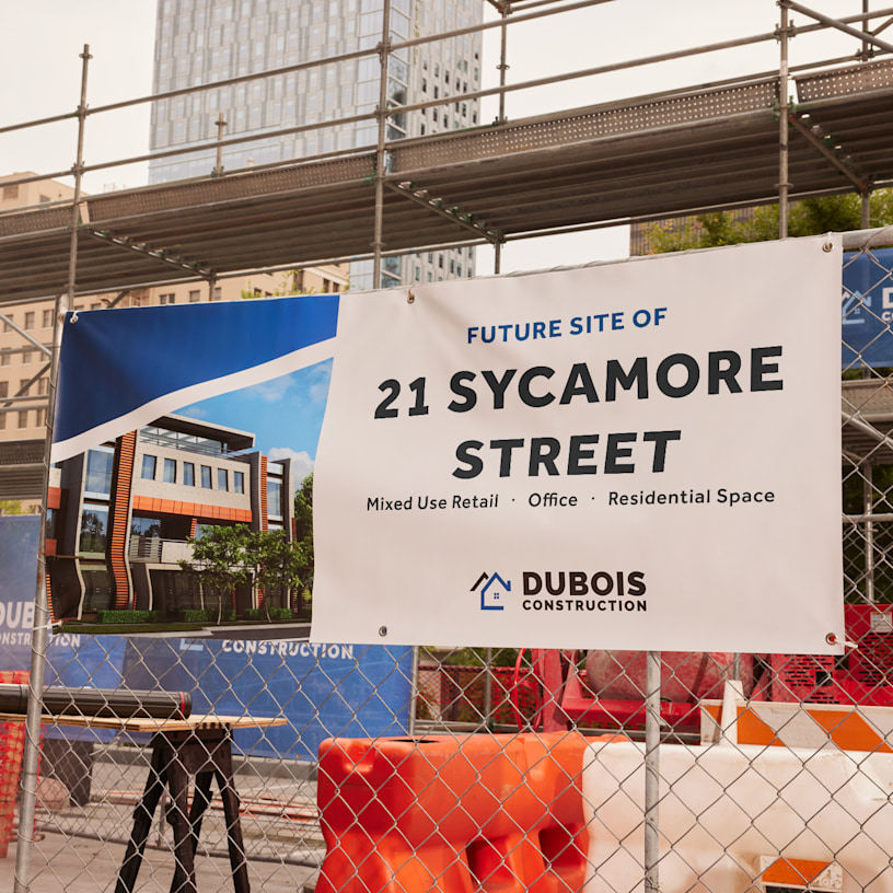 A banner for a construction company tied to a construction site fence, featuring details about the new building.
