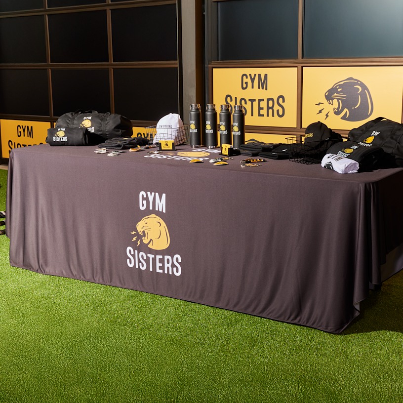 tradeshow rectangle table with branded tablecloth displaying branded apparel and promotional products for a gym business