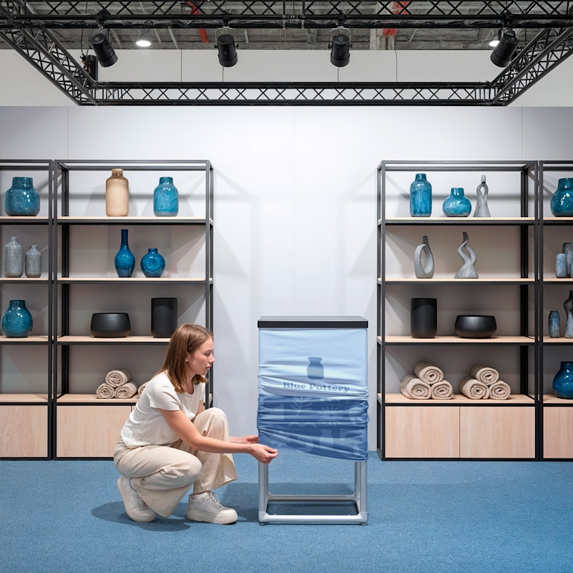 A person setting up their trade show display counter, stretching the fabric onto the frame. 