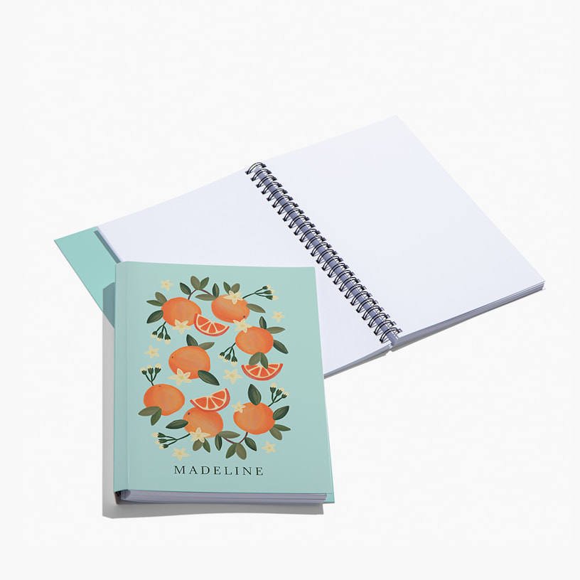 A custom wraparound spiral notebook with blank pages. The cover features illustrated oranges and a person's name. 
