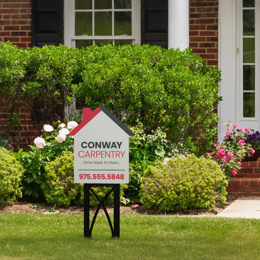 A carpentry yard sign in the shape of a house shown outdoors on a black plastic stand.
