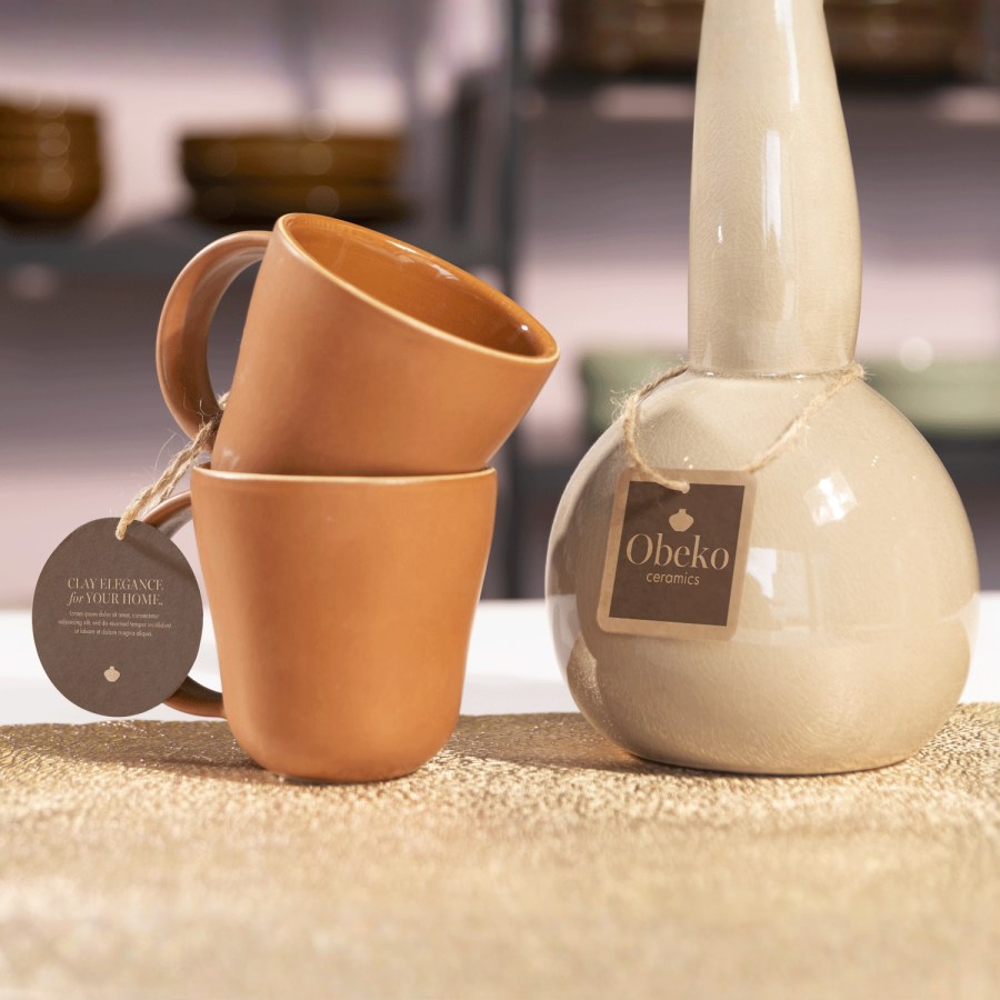 A hang tag tied onto a mug and ceramic container with string.