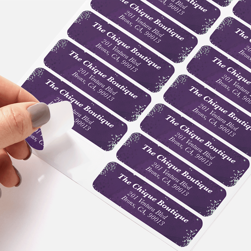 A person peeling a return address label for a boutique from a sheet of labels.