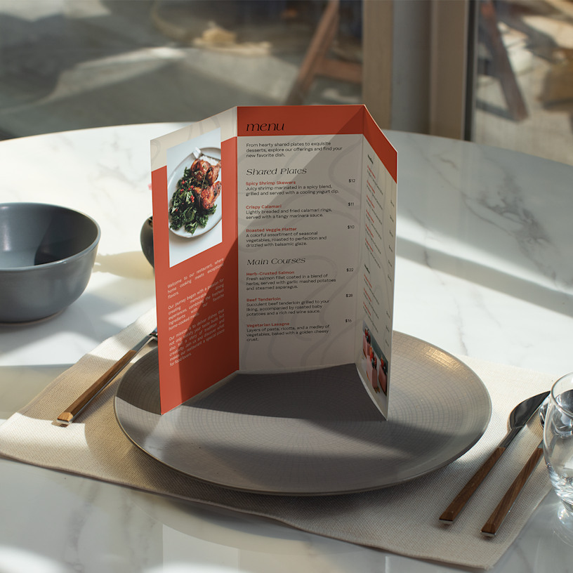 An opened tri-fold menu, standing at a place setting at a restaurant.