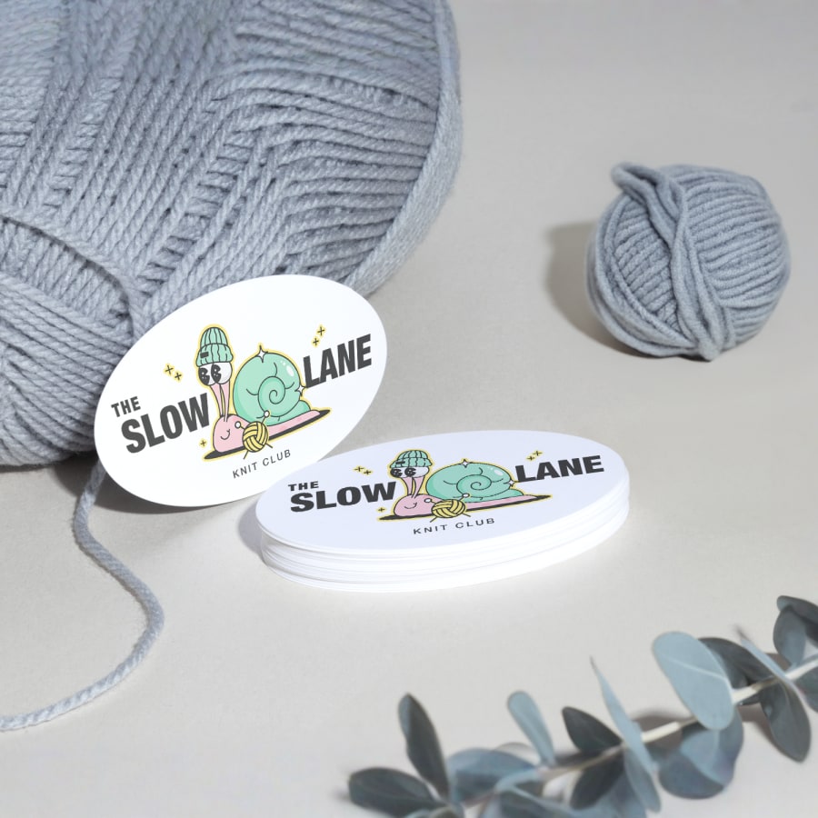 A stack of oval business cards for a knitting club, with yarn and plants in the background.