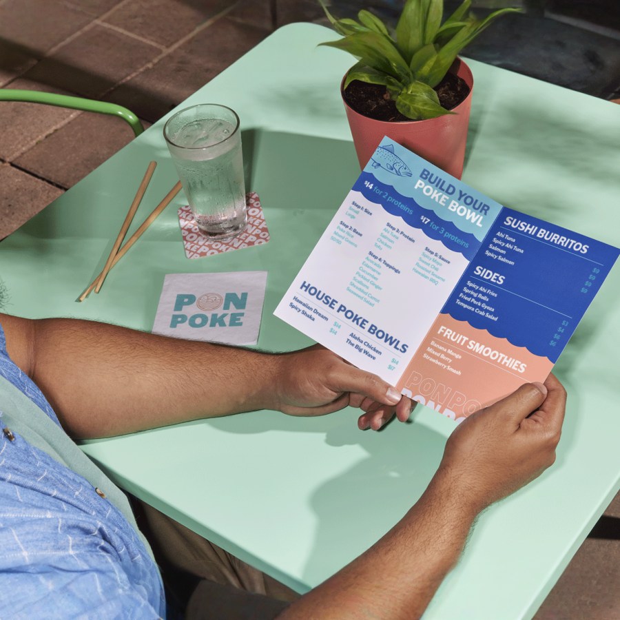 A person sitting at a poke bowl restaurant, reading a bi-fold menu.