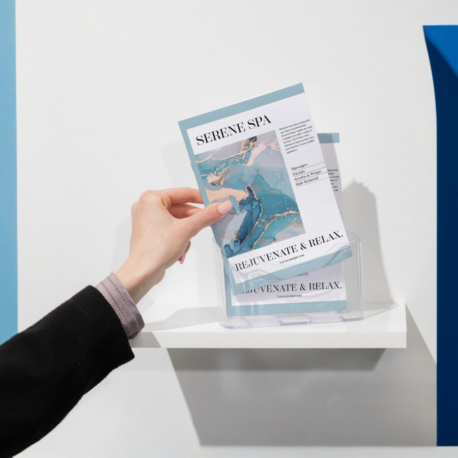 A person takes a saddle-stitch booklet for a spa from a booklet holder. 