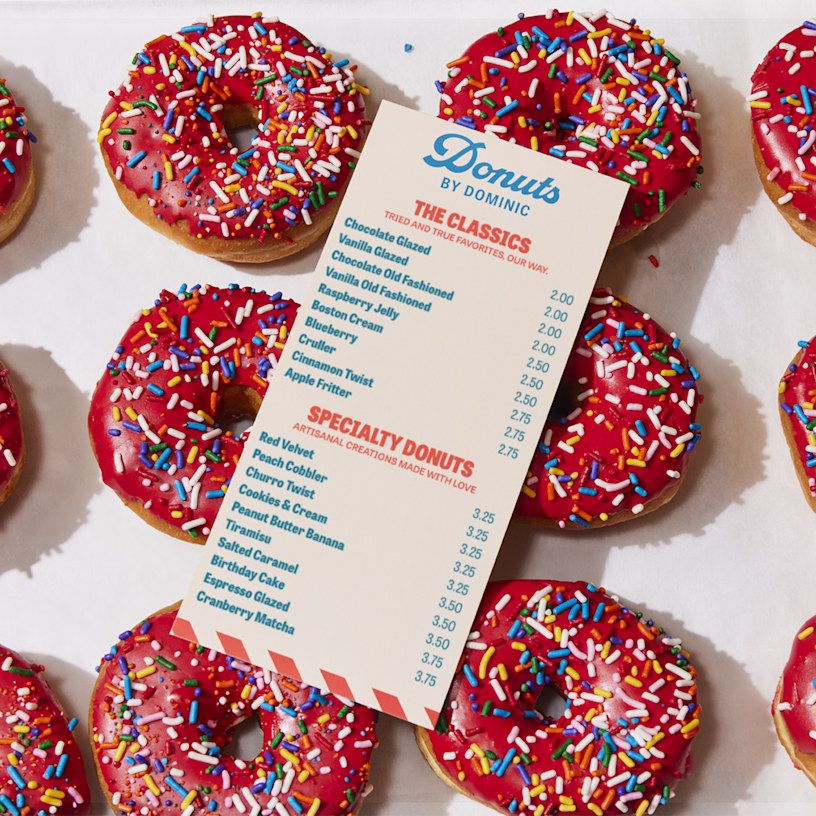A flat menu for a donut shop, resting on a sheet of freshly baked donuts.