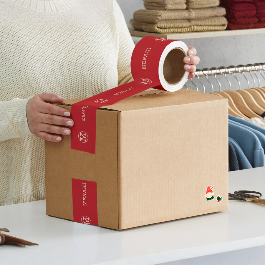 A woman in a white sweater applying white plastic Self-adhesive packaging tape to a cardboard box. The tape is custom printed with a design for a clothing and fashion business.