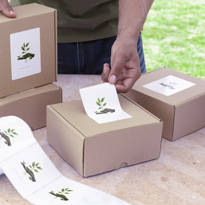 A person applying large rectangular labels from a roll onto boxes of natural skincare products.