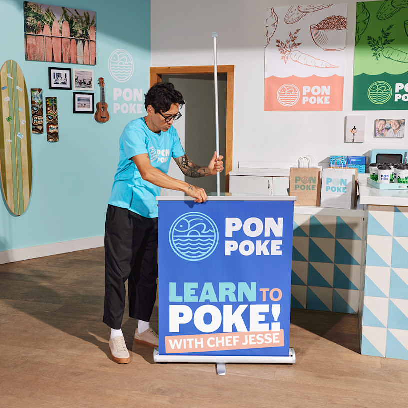 A man setting up his poke bowl retractable banner in a vibrant restaurant setting.
