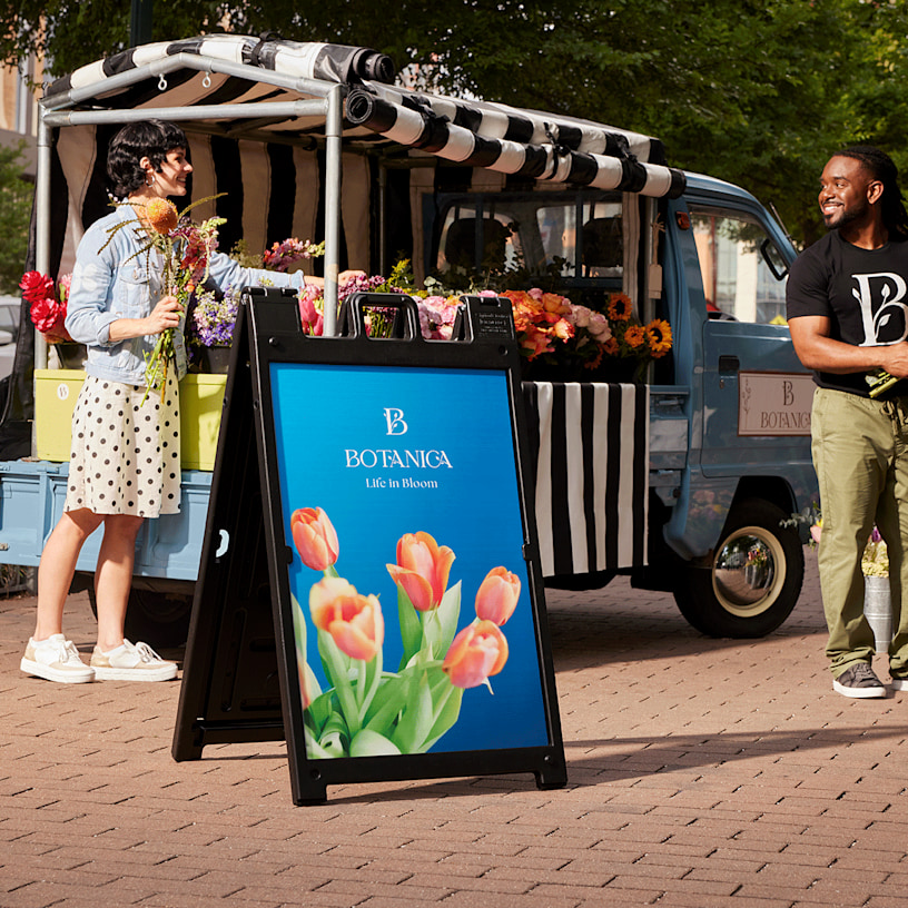 A black Signicade® with a tulip on it in front of a truck selling a variety of flowers.