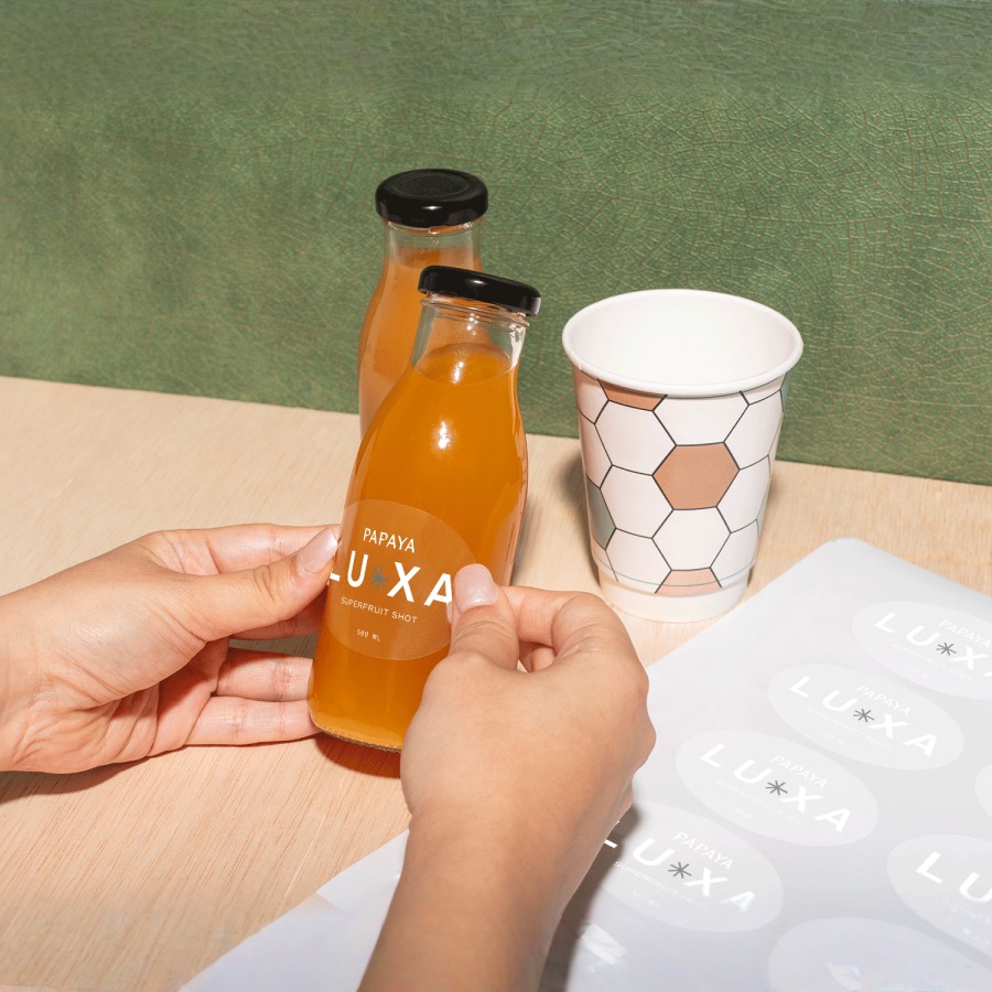 A person applying transparent oval stickers from a sheet on to juice bottles.