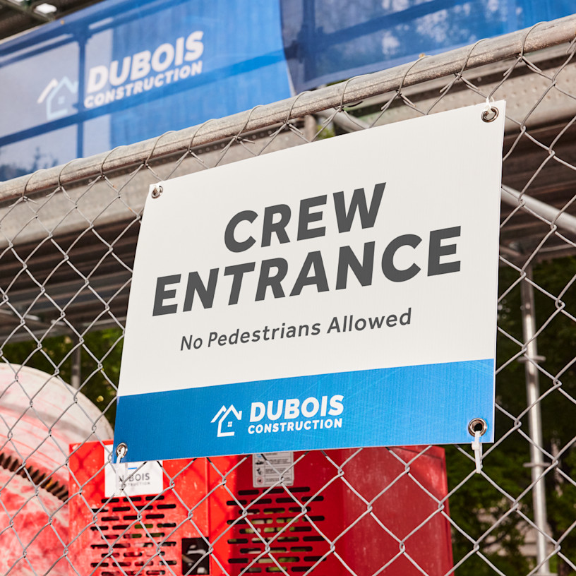 A construction company yard sign with grommets hung up on a fence.