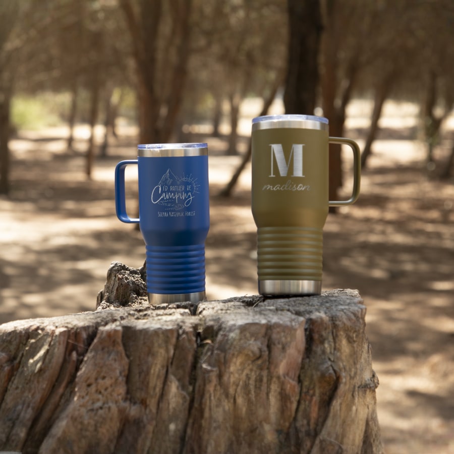 Two custom travel mugs resting perched on a rock in the woods. 