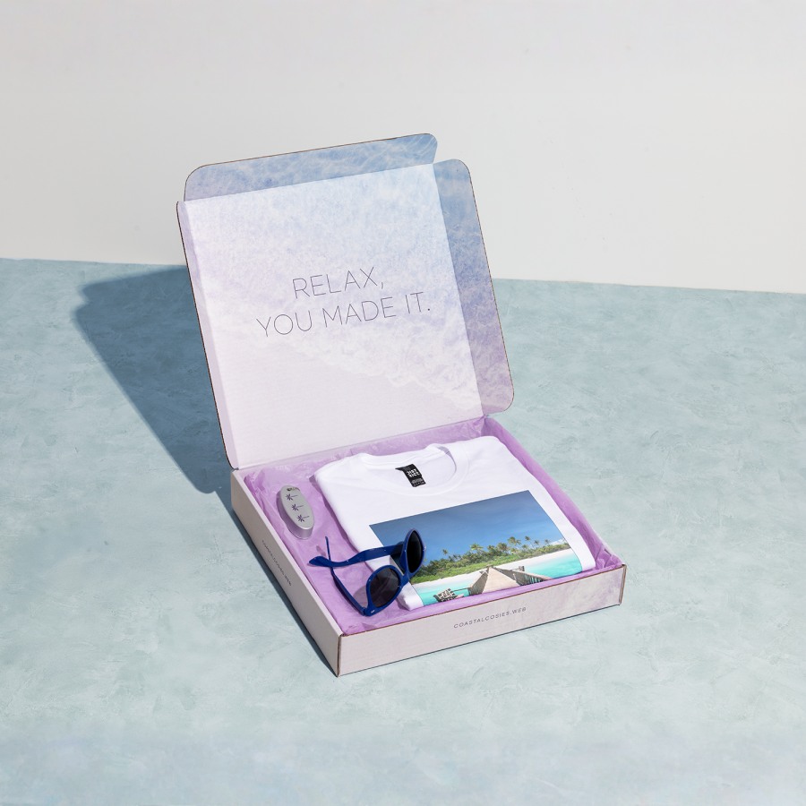 A square mailer box filled with goodies from a travel agency.