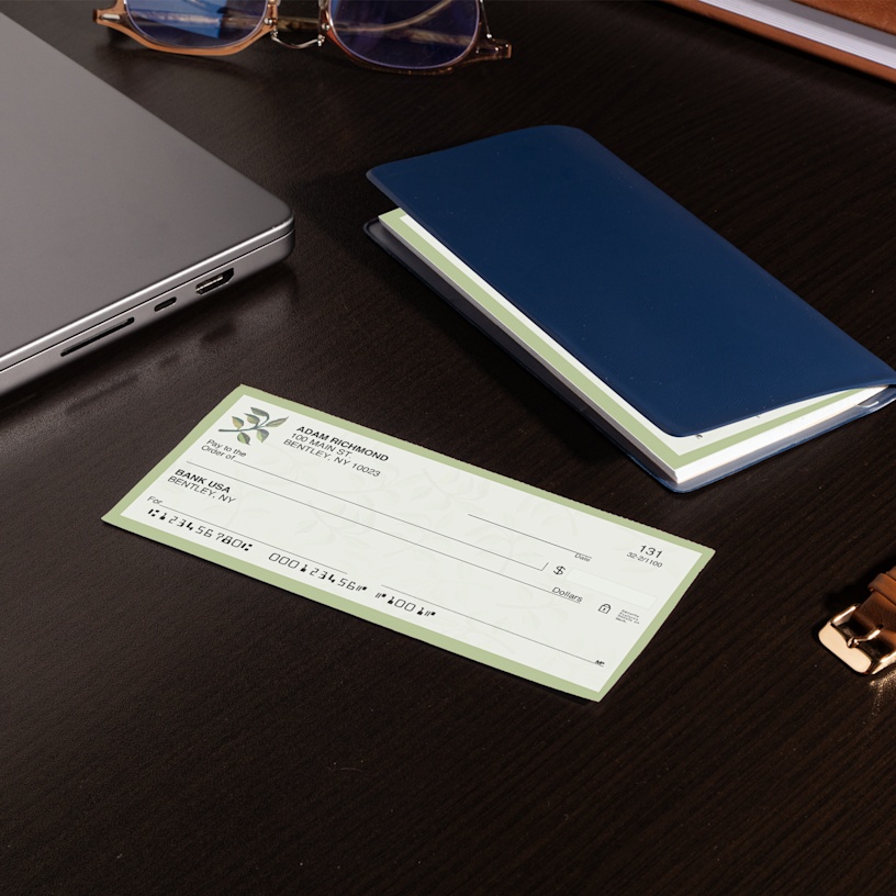 A wallet check on a desk next to a checkbook, laptop and other office supplies.