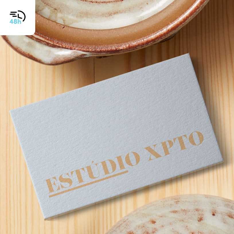 A light gray, textured business card for a ceramics studio on a wooden surface near a ceramic cup, with a 48-hour delivery icon in the corner.