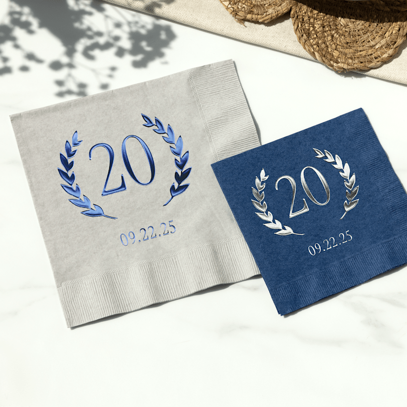Two foil napkins for a birthday, one featuring blue foil and the other featuring silver foil. 