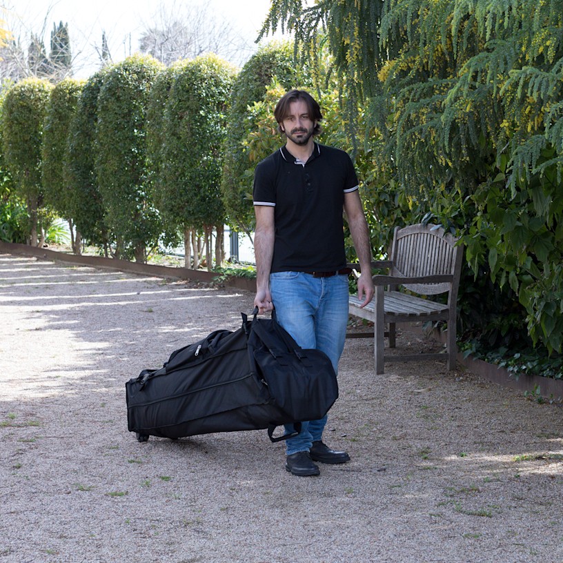 A man wheeling a canopy tent in its carrying case in an outdoor setting.