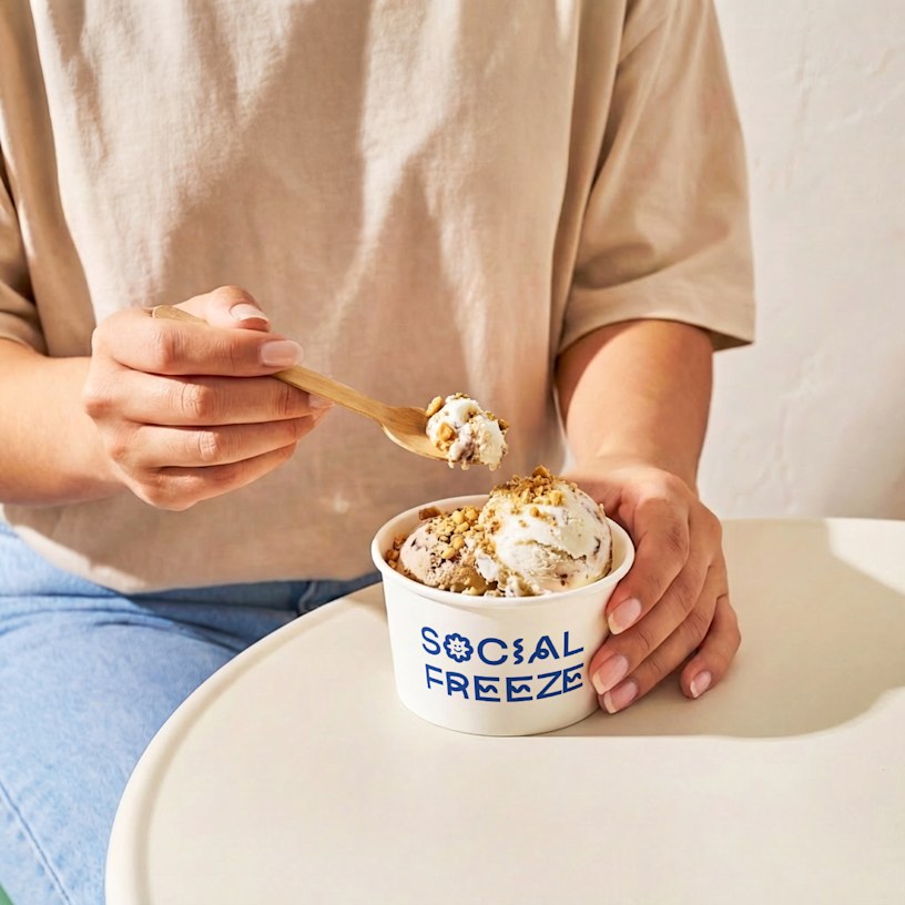 Ice cream with cookie crumbles in a paper cup with a logo on it.