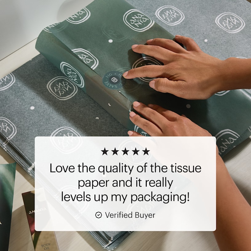 A pair of hands wrapping a gift box in custom printed tissue paper and a customer review: ”Love the quality of the tissue paper and it really levels up my packaging!”