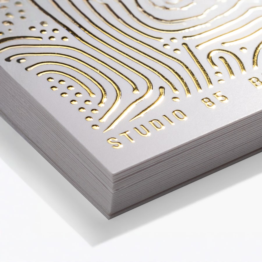 Primer plano de una pila de tarjetas de visita con relieve metalizado dorado y esquinas cuadradas.