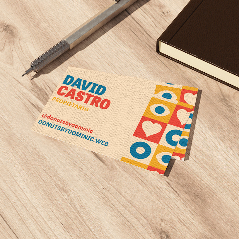 Una pila de tarjetas de visita con acabado lino de una tienda de dónuts, colocada sobre una superficie de madera junto a una libreta y un bolígrafo.