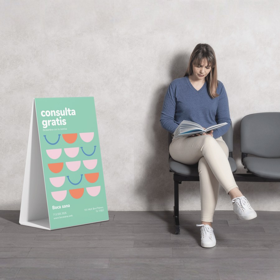 La imagen de una mujer con una blusa azul leyendo mientras está sentada en una sala de espera, con un caballete publicitario corrugado promocionando una consulta gratis con el dentista.