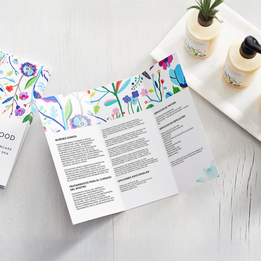 Folletos trípticos de una empresa de cuidado de la piel se muestran sobre una superficie blanca, junto a algunos productos para el cuidado de la piel.