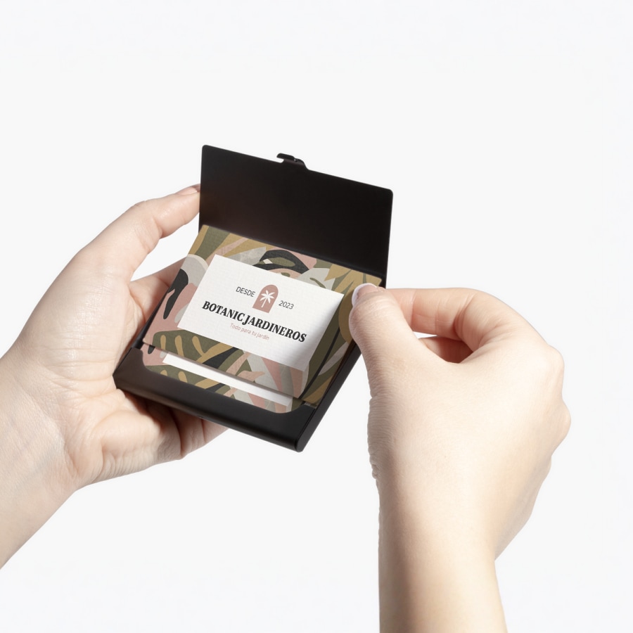 Una persona sujetando un tarjetero de aluminio negro mostrando tarjetas de presentación de una empresa de jardinería.