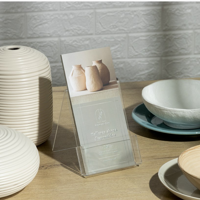 Un conjunto de tarjetas informativas con relieves metalizados plateados de un estudio de cerámica. Las tarjetas informativas están en un soporte plástico rodeado de artículos cerámicos.