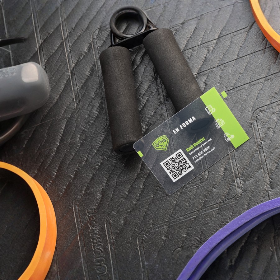 Una tarjeta de presentación de plástico transparente de un entrenador personal con equipo de ejercicios en el fondo. 