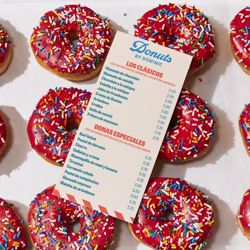 Un menú plano de una tienda de donas, colocado sobre una hoja de donas recién horneadas.