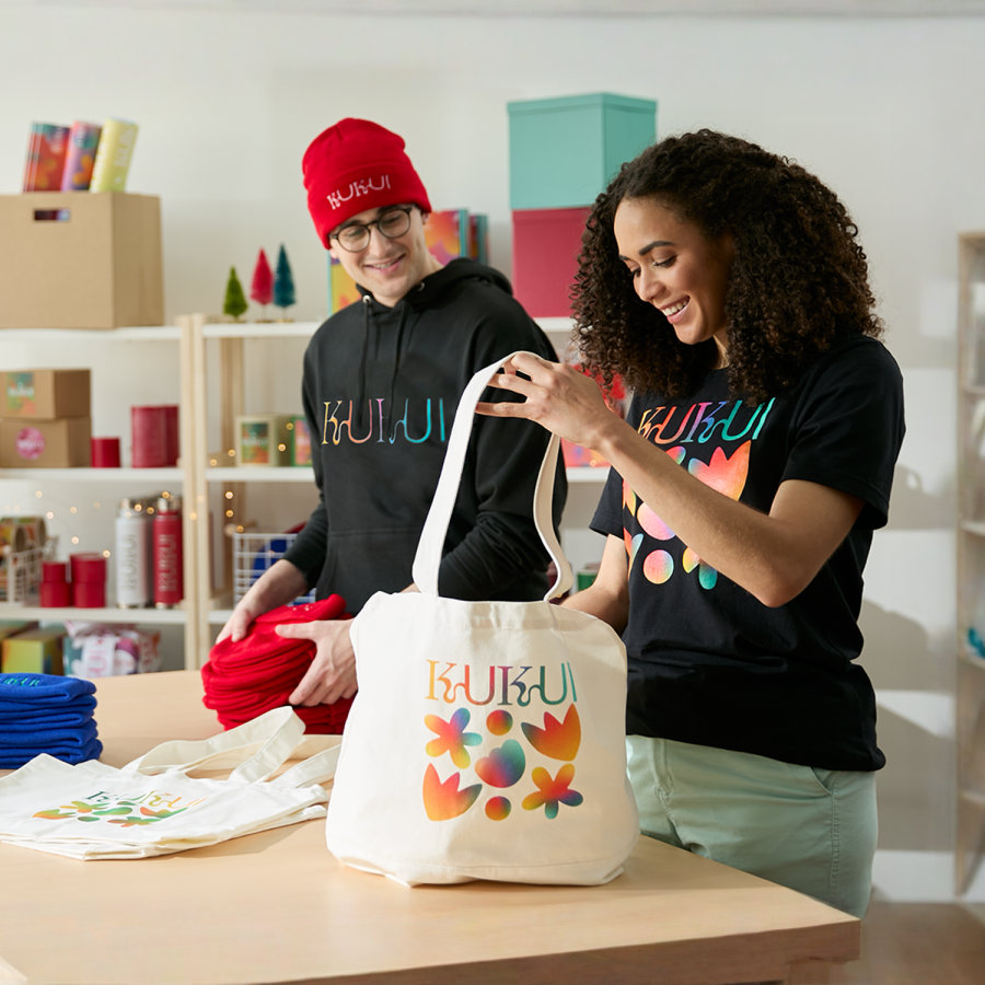 Dos empresarios de una pequeña empresa empaquetan bolsas de tela personalizadas con gorritos personalizados y otros artículos. 