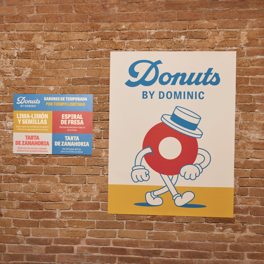 Un póster horizontal al lado de uno vertical en una pared de ladrillos que muestran una tienda de donas.