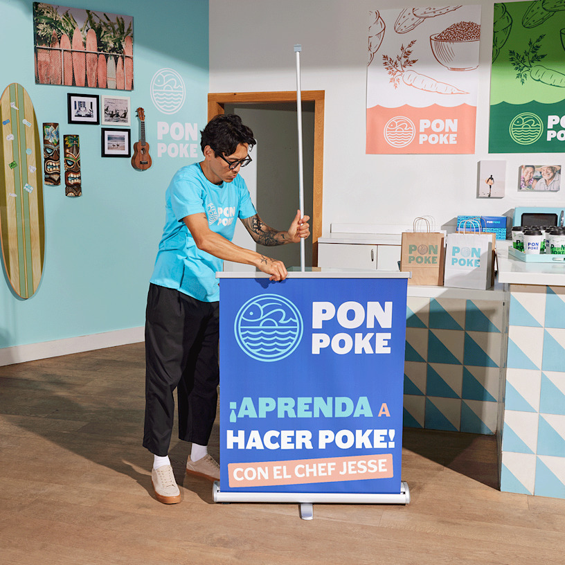 Un hombre está colocando su lona retráctil con un tazón de poke en un restaurante vibrante.