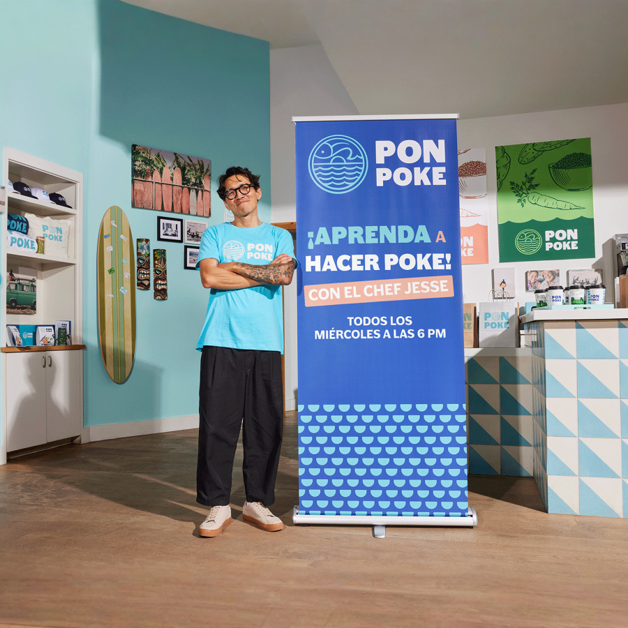 Un hombre está orgullosamente de pie junto a su lona retráctil con un tazón de poke.