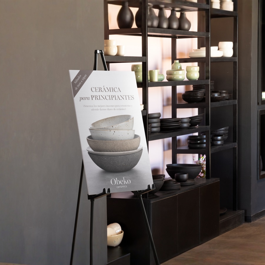 Un cartel de cartón pluma en un caballete junto a un estante en una tienda de cerámica.