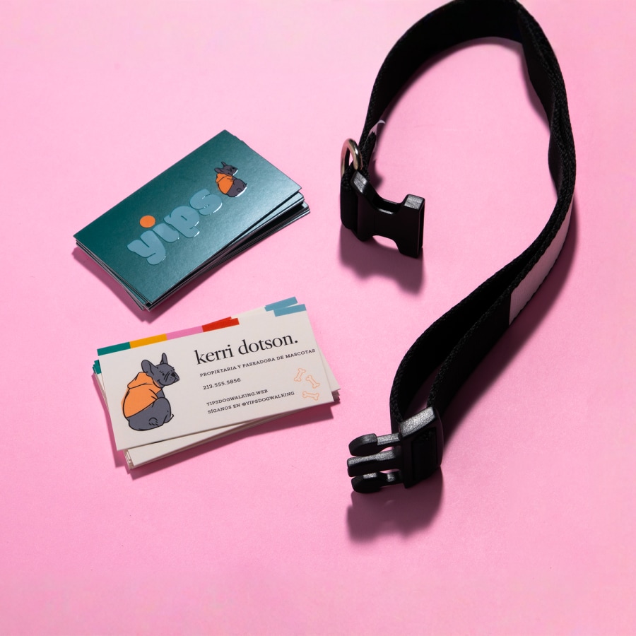 Dos conjuntos de tarjetas de presentación con relieves brillantes, mostrando la parte de adelante y atrás del diseño de una empresa de paseadores de perros. Un collar de perro está a la par de éstas.