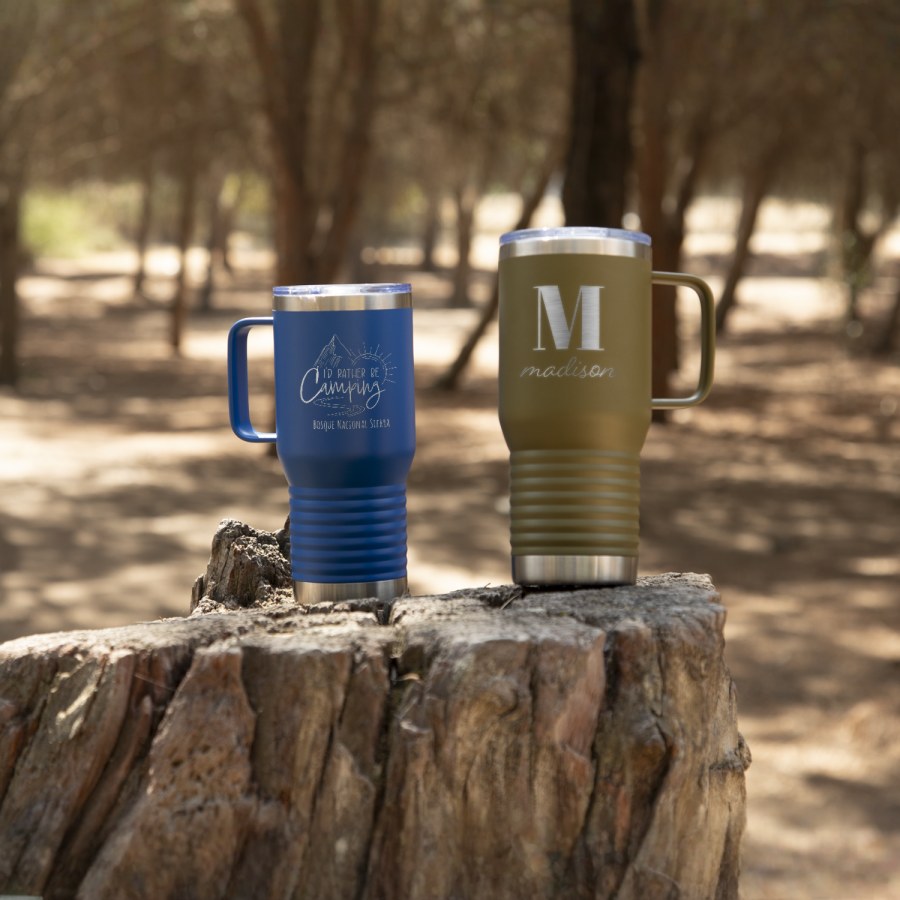 Dos tazas de viaje personalizadas sobre una roca en los bosques. 