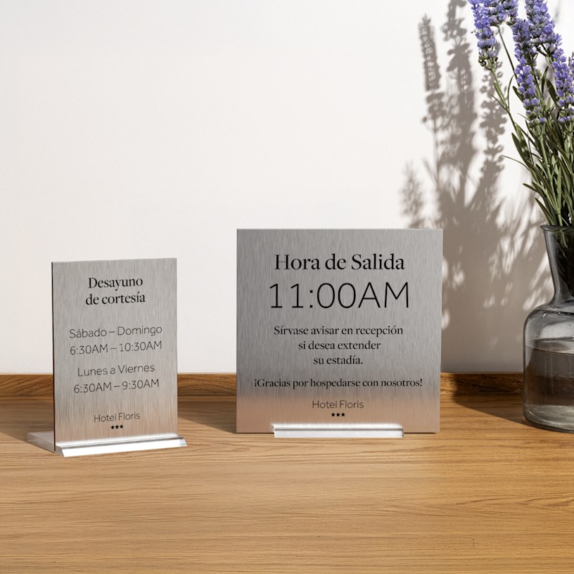 2 carteles metálicos para mesa de hotel, uno al lado del otro. 1 indica el horario del desayuno de cortesía y el otro, la hora de salida.