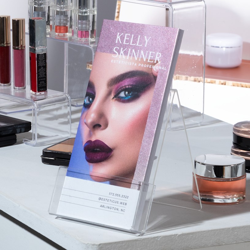 Se muestran tarjetas informativas con efecto metálico resplandeciente morado de un maquillista, colocadas en el mostrador de un salón de belleza.