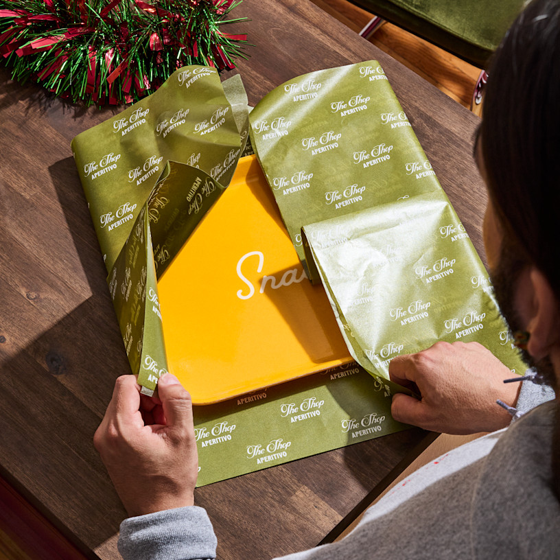 A woman wrapping a yellow gift box in tissue paper customized for an Italian restaurant.